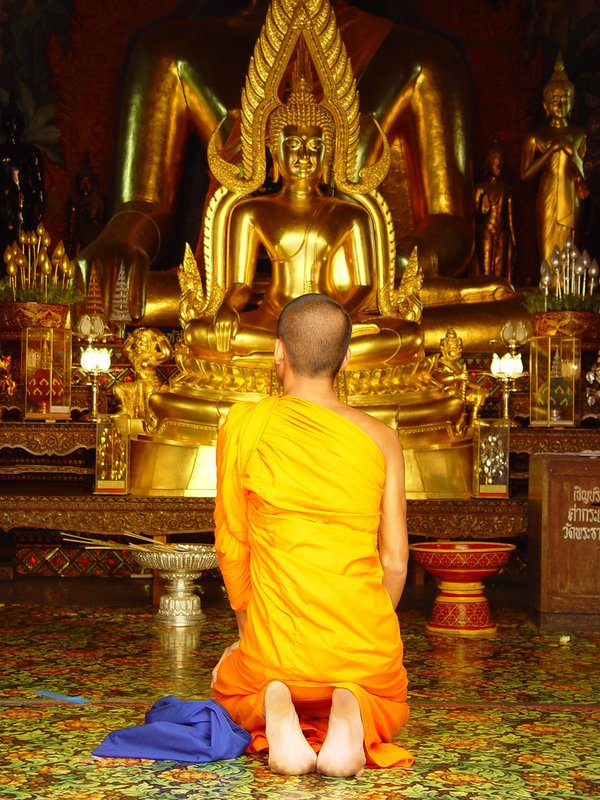 buddhistischer Mönch kniet vor der Buddha Statue